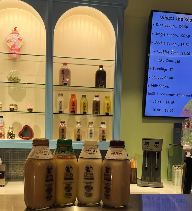Bottles of ice cream and toppings on a counter with a menu display in the background.