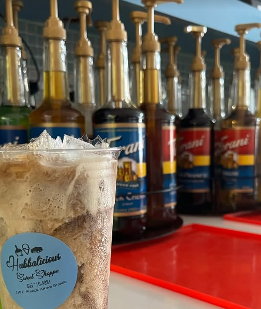 Ice cream float with a Hubblicious Sweet Shoppe label in front of liquor bottles.