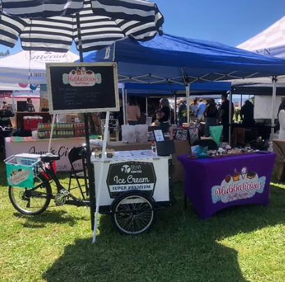 Ice cream cart and vendor setup at an outdoor event with striped umbrellas and a blue canopy.