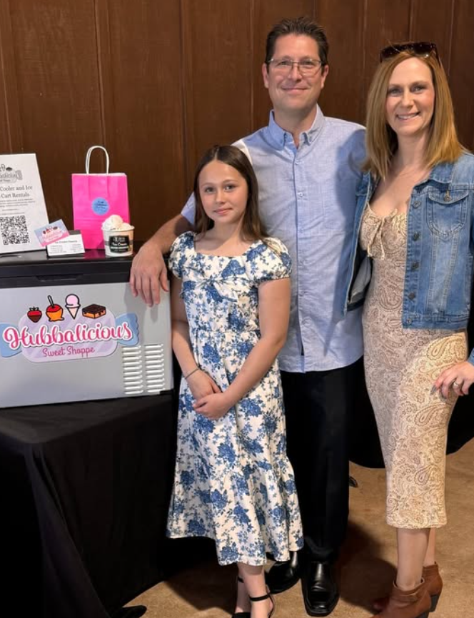 Family of three standing in front of a branded booth at an event.