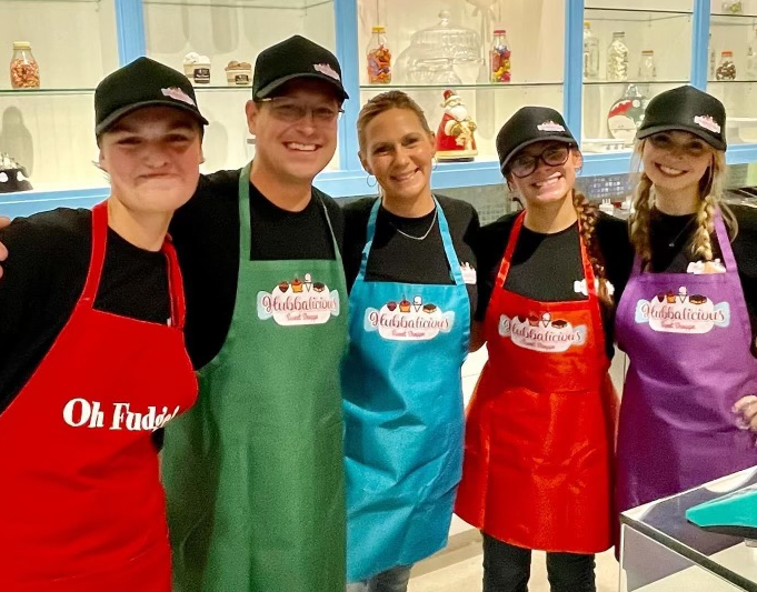 Five people wearing colorful aprons with 'Oh Fudge!' branding in a kitchen setting.